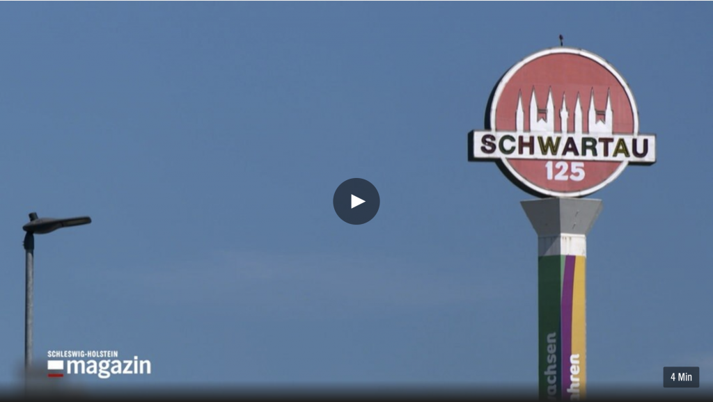 Das Logo der Schwartauer Werke auf einem sich drehenden Schild vor blauem Himmel