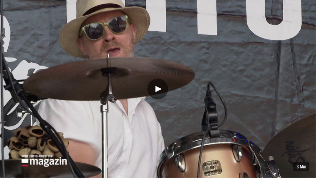 Mann mit Sonnebrille und Hut an Schlagzeug